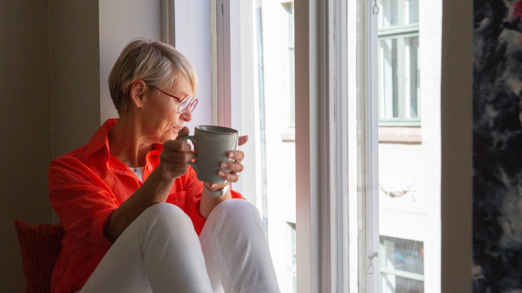 Kvinna som dricker te och tittar ut genom fönster. Mediedrev.