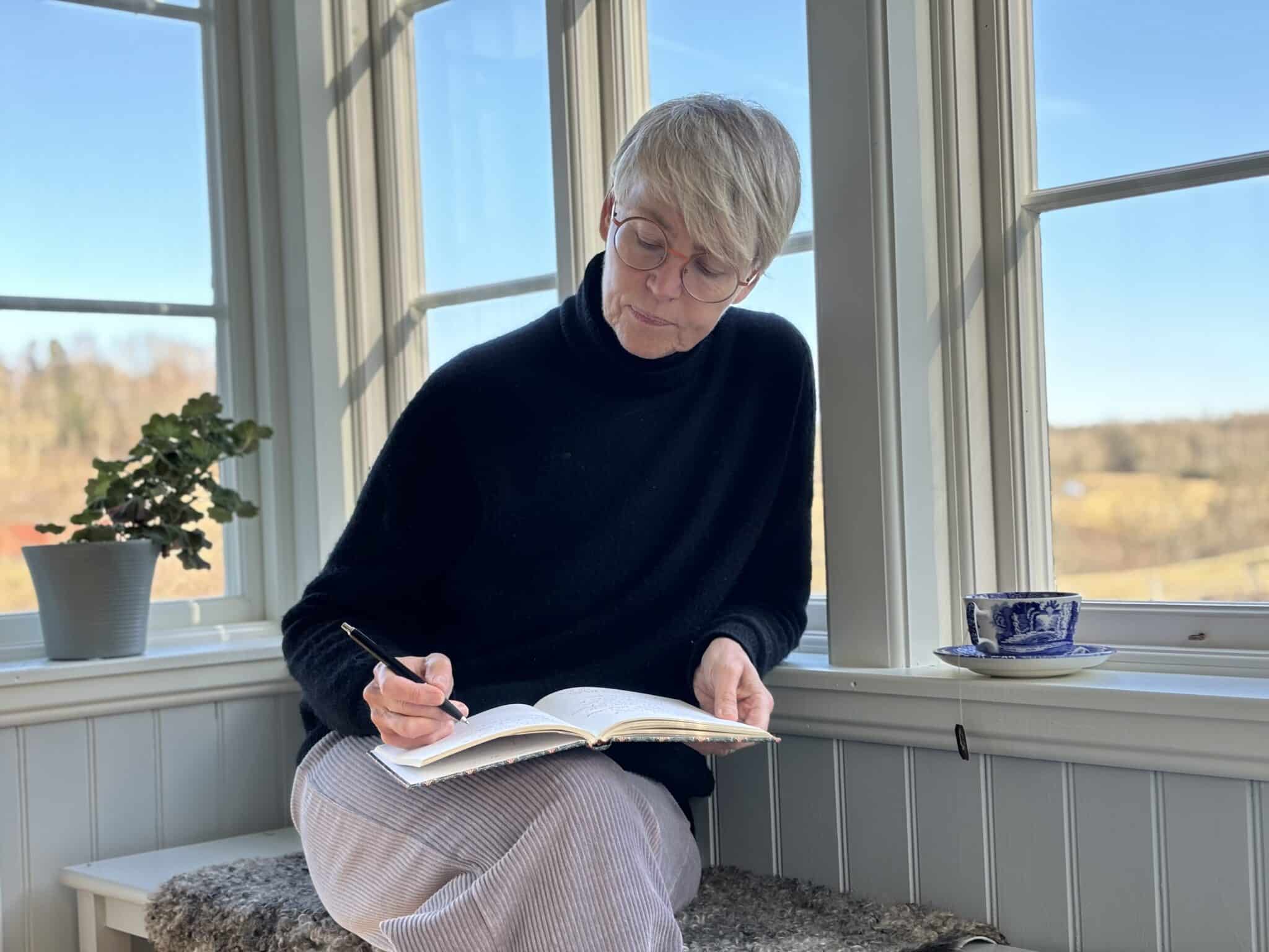Kvinna sitter på en veranda och skriver dagbok.